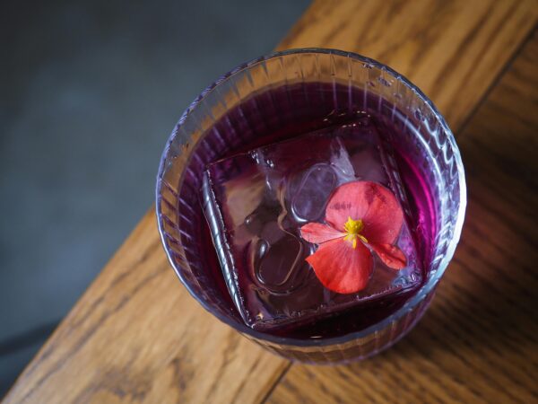 Close-up of a purple cocktail with an ice cube and flower, perfect for bar menus.